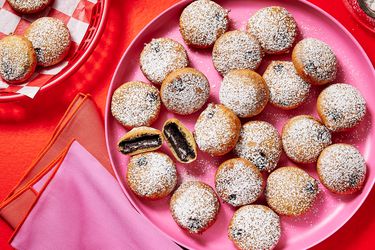 pink platter of fried oreos, two with bite taken out and middle showing. Red background and red basket of oreos on the side, and pink and red napkins. 