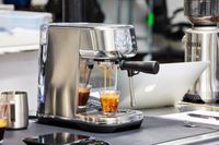 Breville Bambino Plus Espresso Machine making espresso coffee with nearby laptop