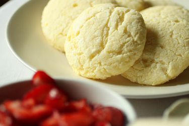 Closeup of gluten free short cakes on a plate. A bowl of strawberries is in the foreground, blurred by the narrow depth of field.