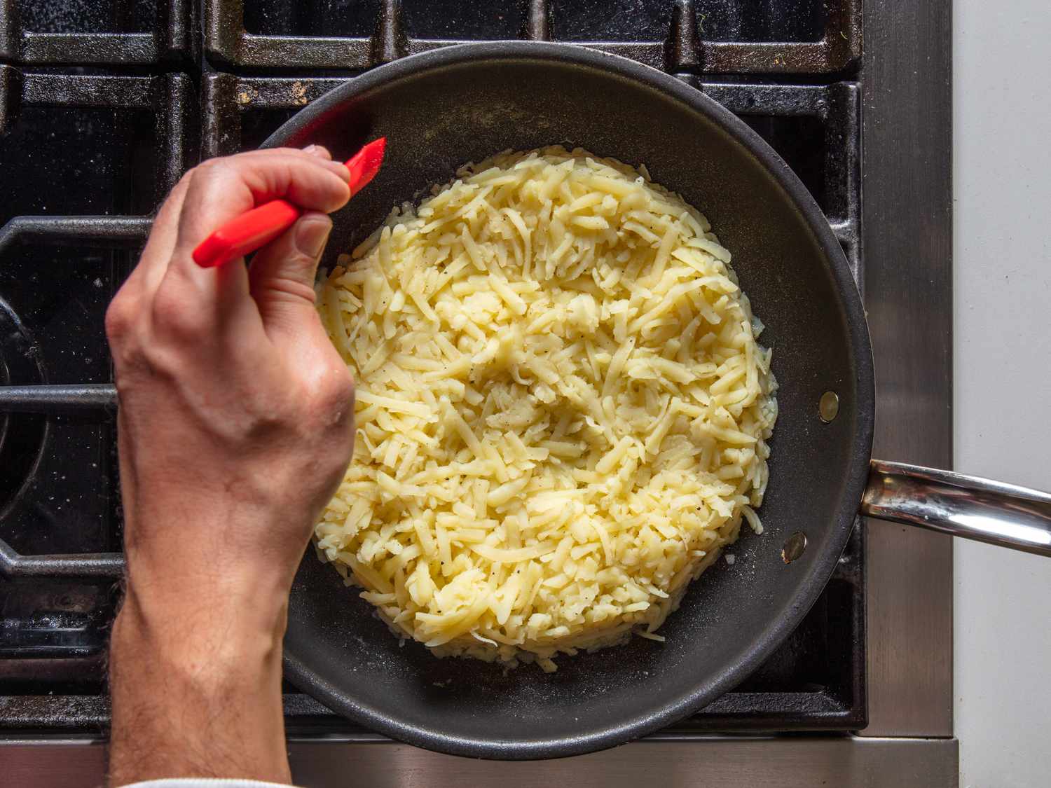 Shaping the cooked shredded potato into a round cake shape with a spatula.