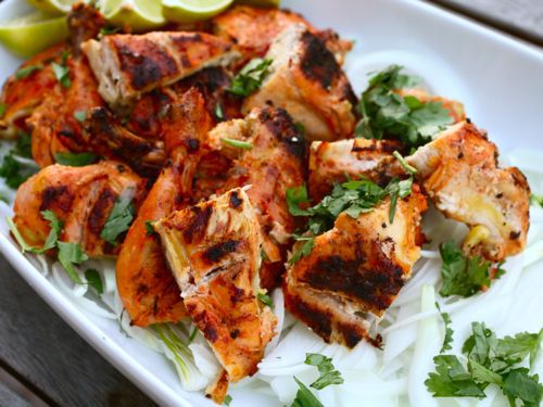 Close-up of the grilled tandoor-style Cornish hen on a platter, cut up in serving pieces and sprinkled with cilantro.
