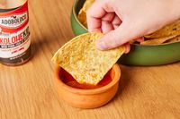 Person dipping chip in bowl of Adoboloco Island Wings Pineapple Cayenne Pepper Sauce