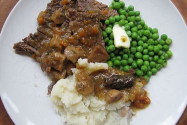 Pot roast on a white plate with buttered peas, mashed potatoes and gravy. 