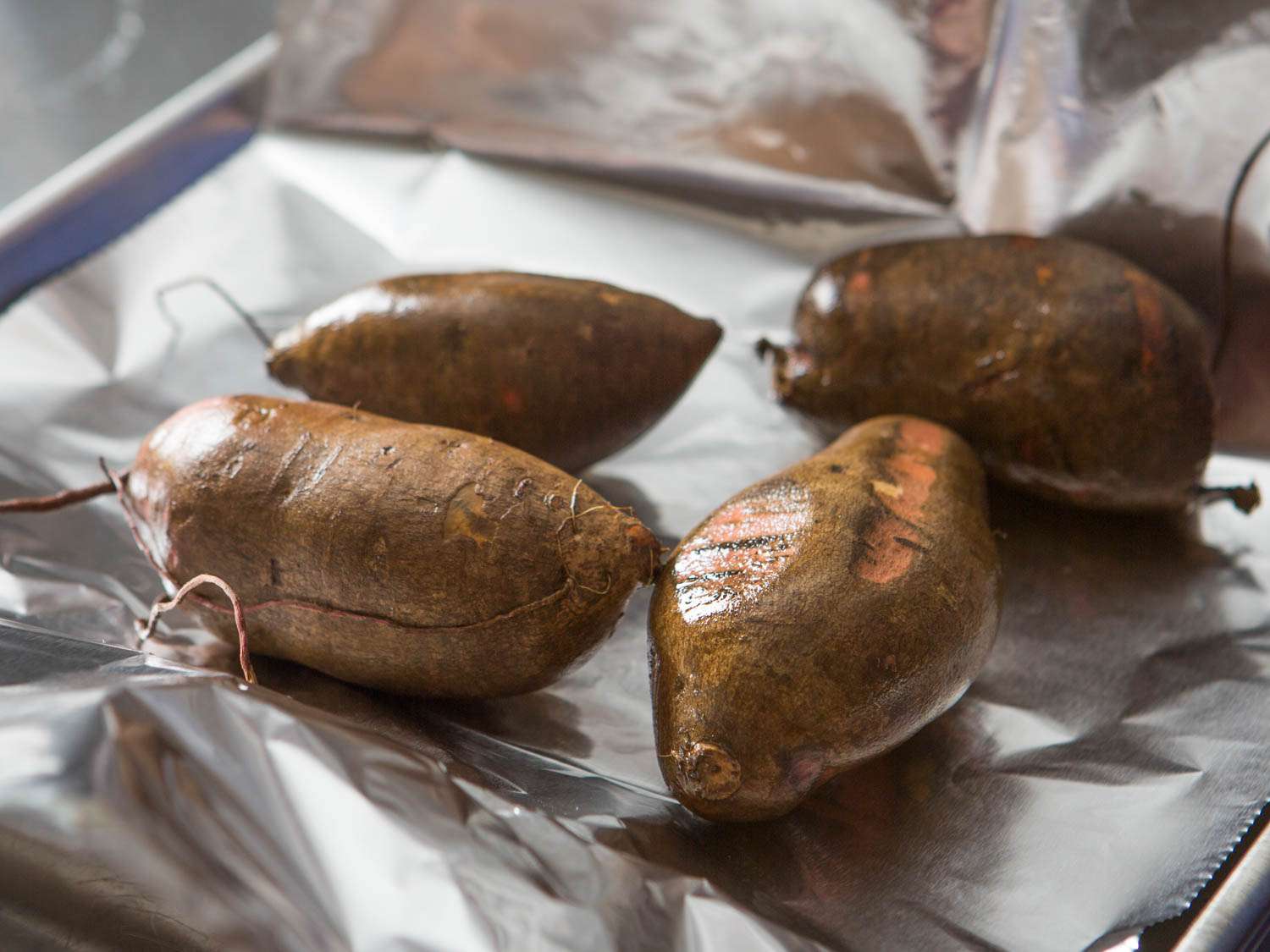 Whole sweet potatoes on a foil-lined rimmed baking sheet