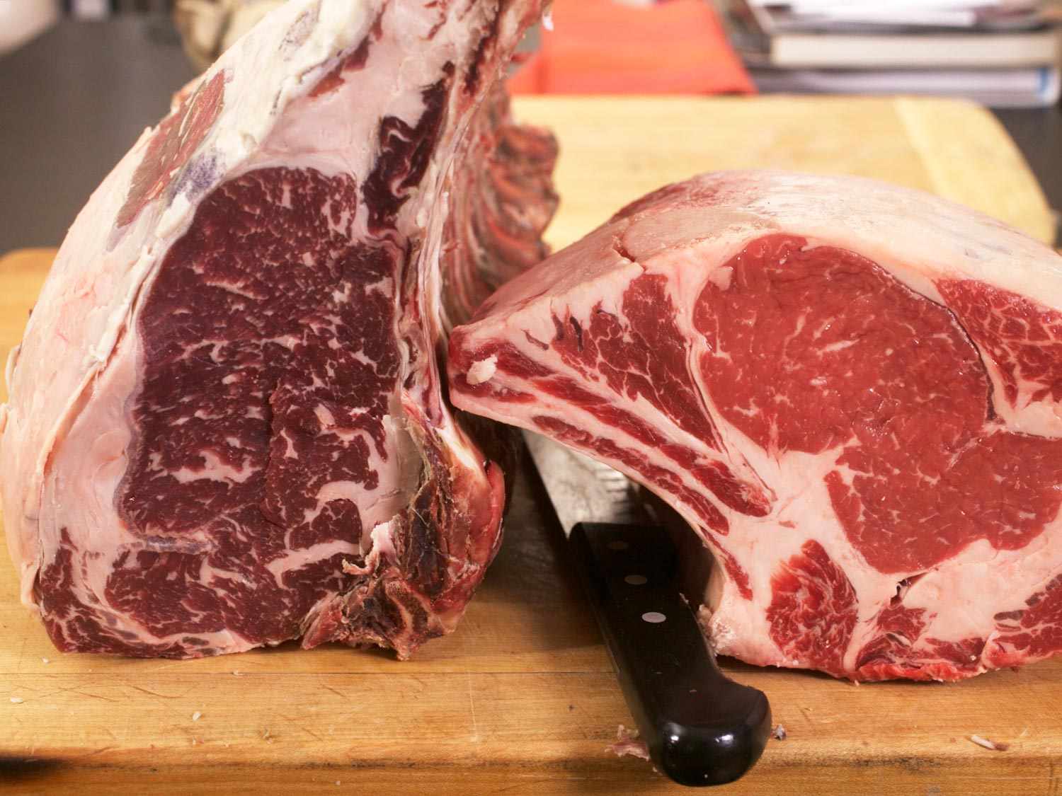Two prime rib roasts placed next to each other on a cutting board. The one on the left is darker and has a purple hue.
