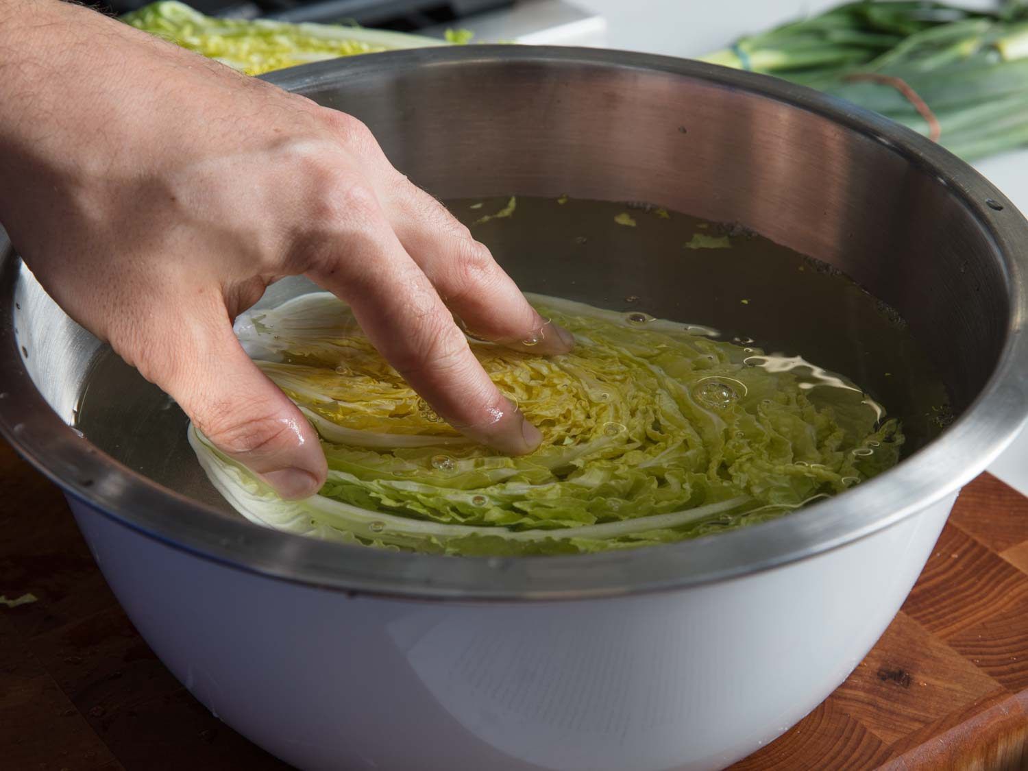 A hand pressing down Napa cabbage in a stainless bowl for Korean bossam.