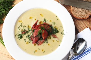 Overhead shot of a white bowl filled with creamy potato and leek soup topped with fried kielbasa slices.