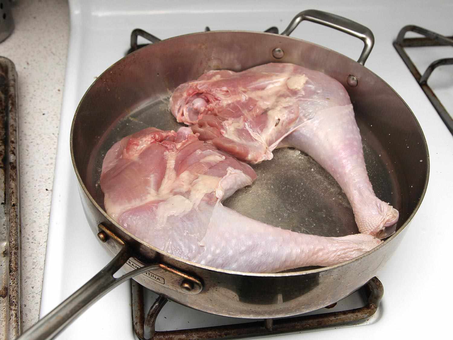 Two turkey legs searing in a saute pan.