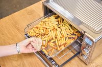 A person removes a basket of fries from the Breville The Smart Oven Air Fryer Compact