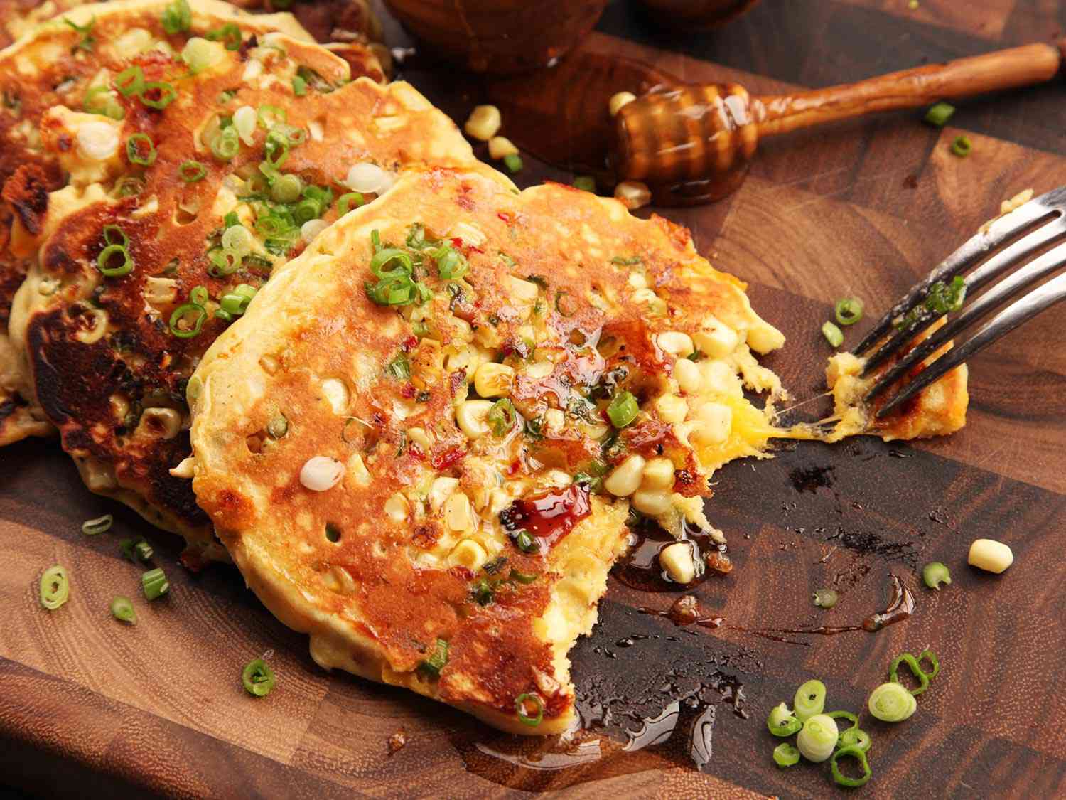 Fork exposing melted cheddar from interior of savory pancakes with bacon, corn, jalapeños, and scallions 