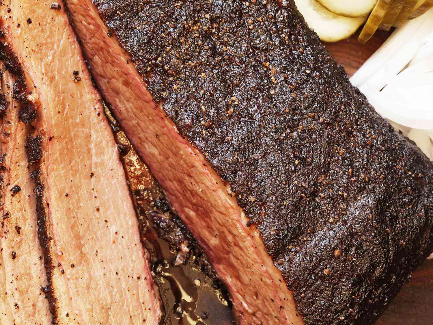 Close-up of finished brisket with thin slices removed, juice pooling in between slices