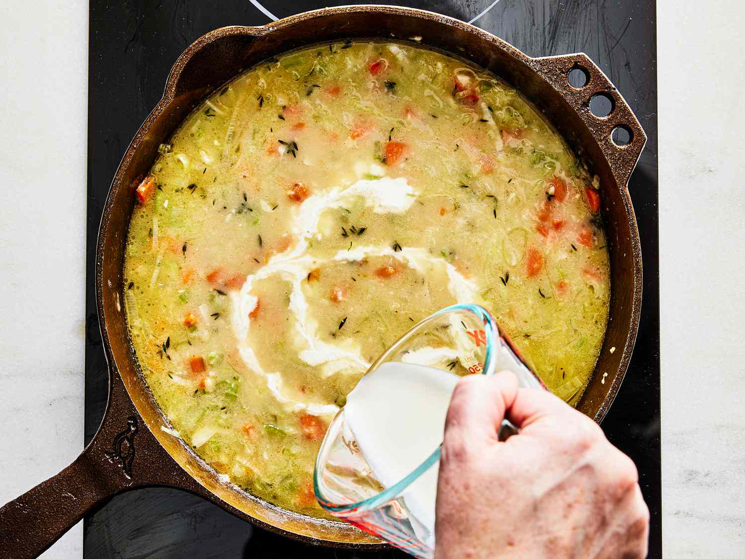 Broth and cream added into skillet of cooked vegetables in skillet 