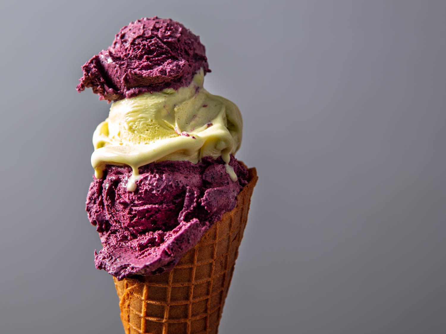 Waffle cone filled with scoops of blueberry and pistachio ice cream.