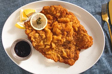 Plate of wienerschnitzel with lemon slices and dark sauce on the side