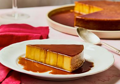 A slice of orange and saffron flan on a plate with caramel sauce placed beside a full flan serving in the background