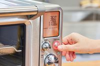 A thumb touching a button on the Breville the Smart Oven Air Fryer