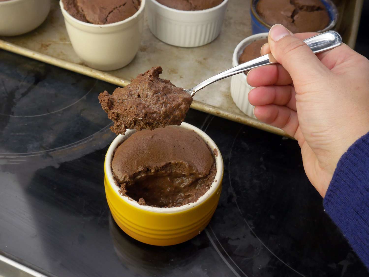 a person taking a scoop of chocolate souffle from the le creuset ramekin