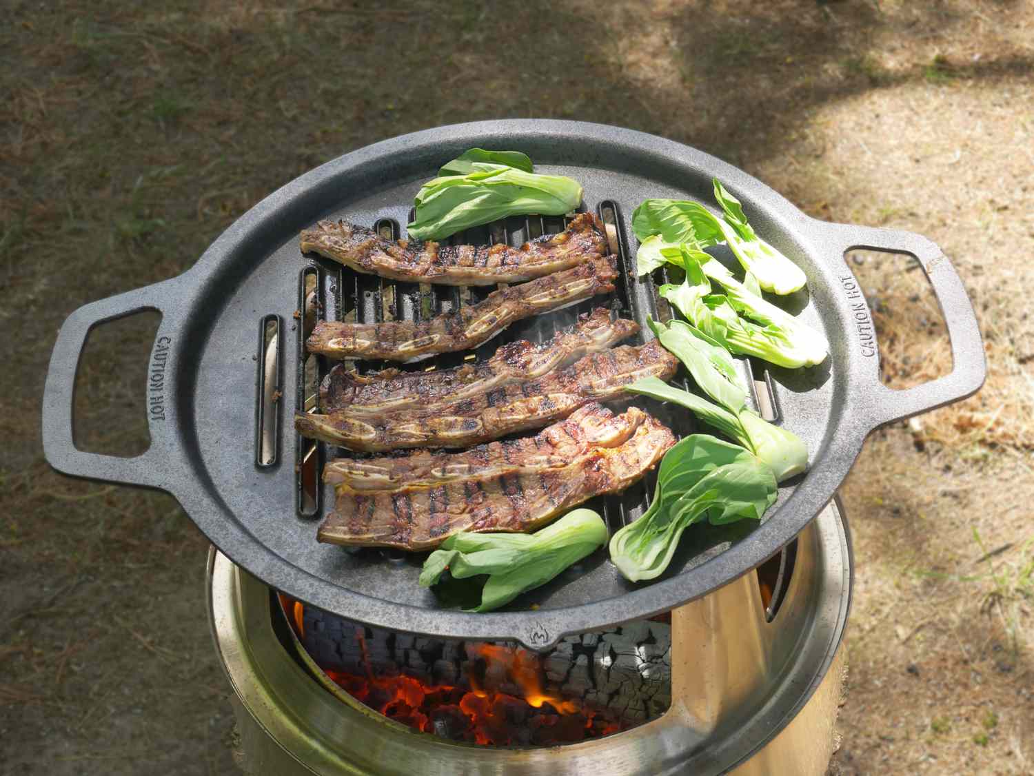 Korean short ribs and baby bok choi cooking on a cast iron grill grate on the solo stove