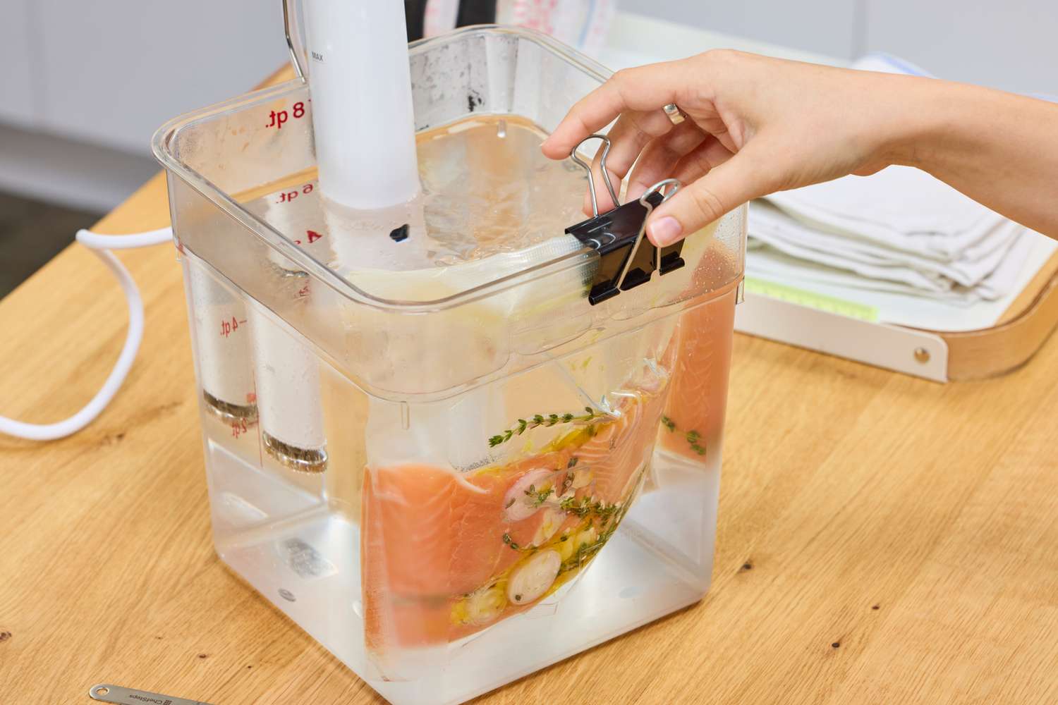 Breville Joule Turbo Sous Vide Machine setup with a hand holding a bag containing food and herbs immersed in water