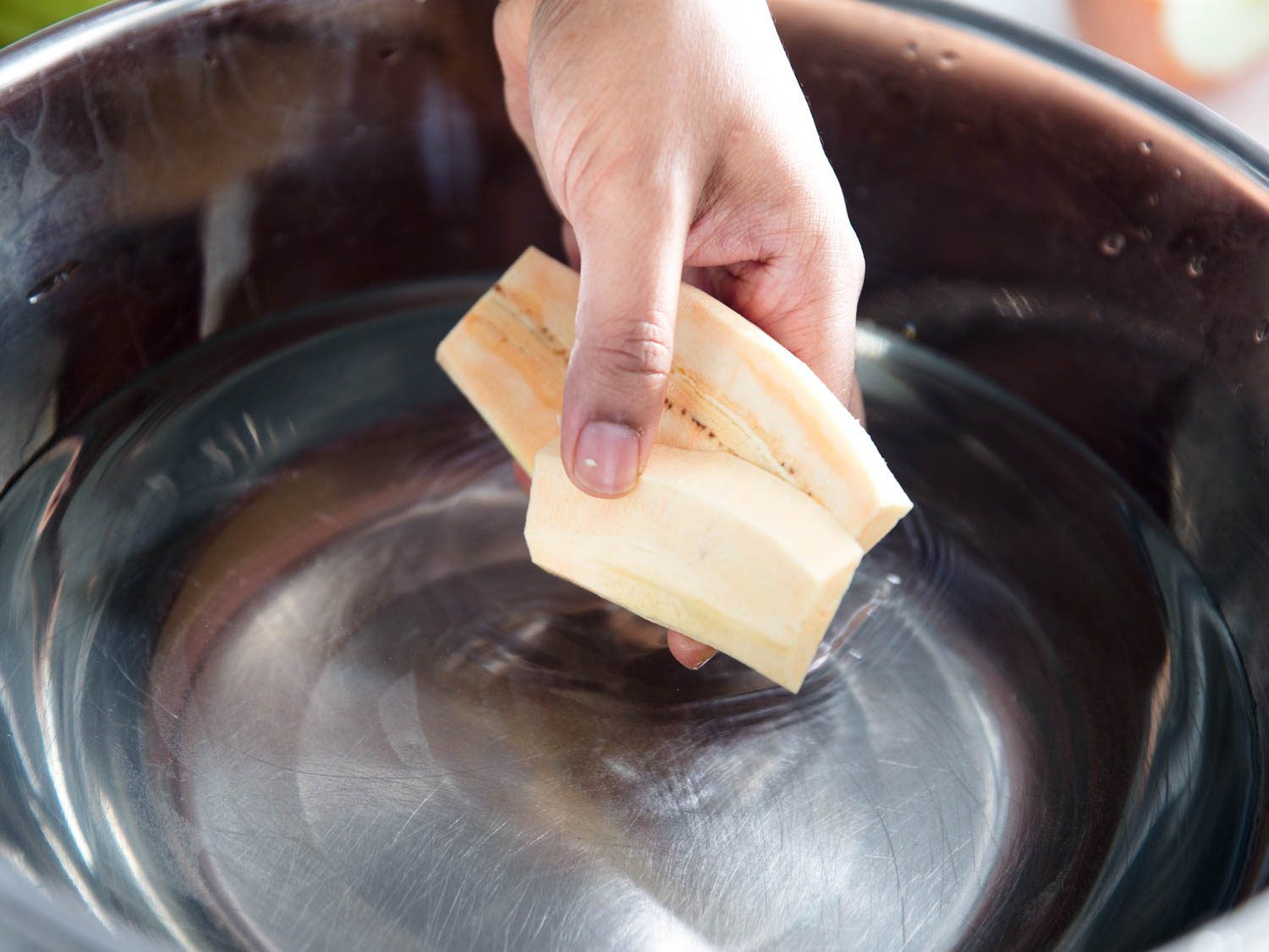 Dropping cut and prepared plantains into a salt brine to prevent oxidation.