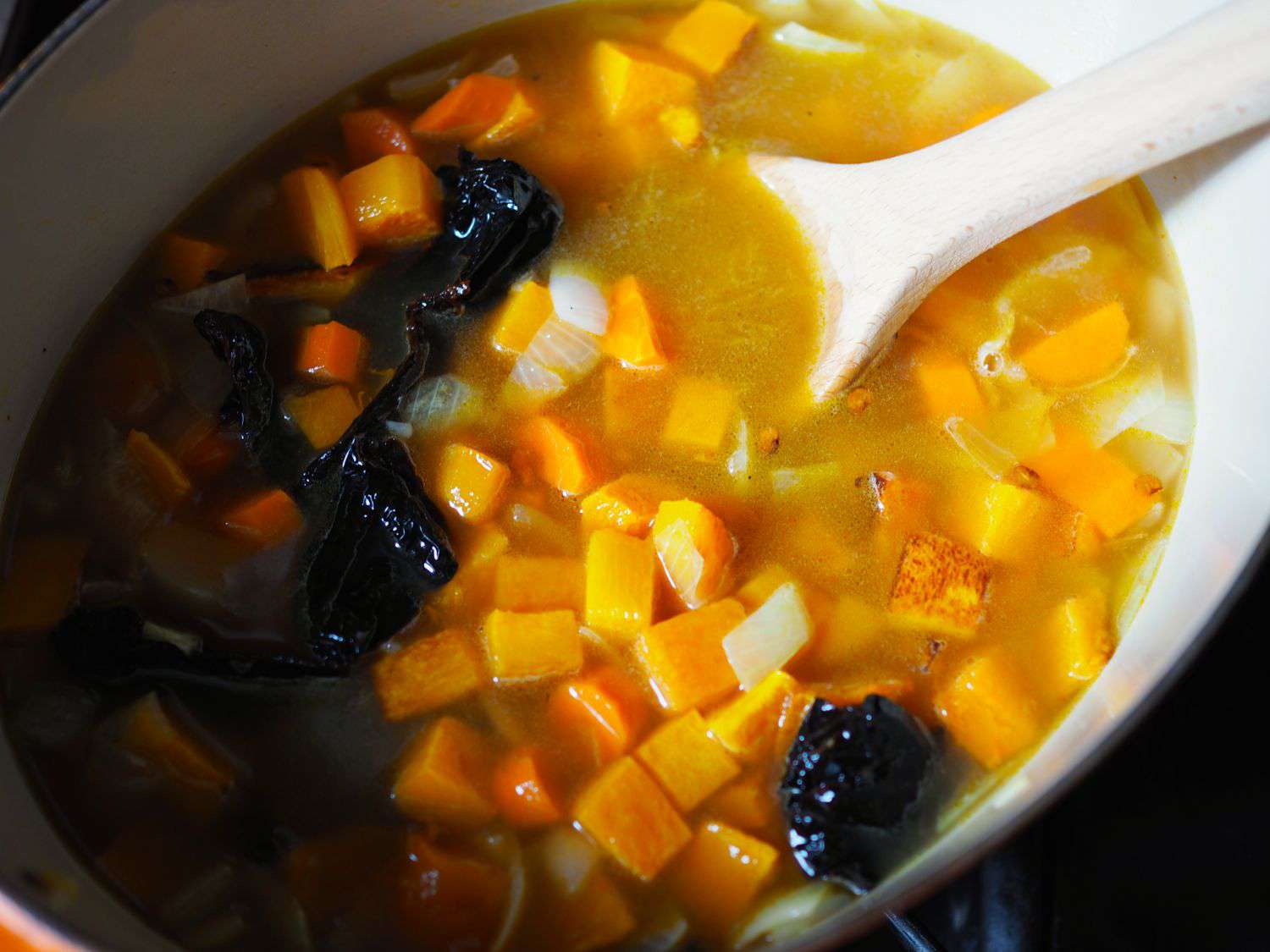 Butternut squash, onion, and ancho chiles simmering in chicken stock in a Dutch oven. 
