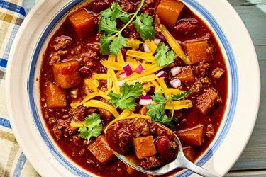 A bowl of turkey chili with squash beans cheese onions and cilantro garnish spoon served alongside