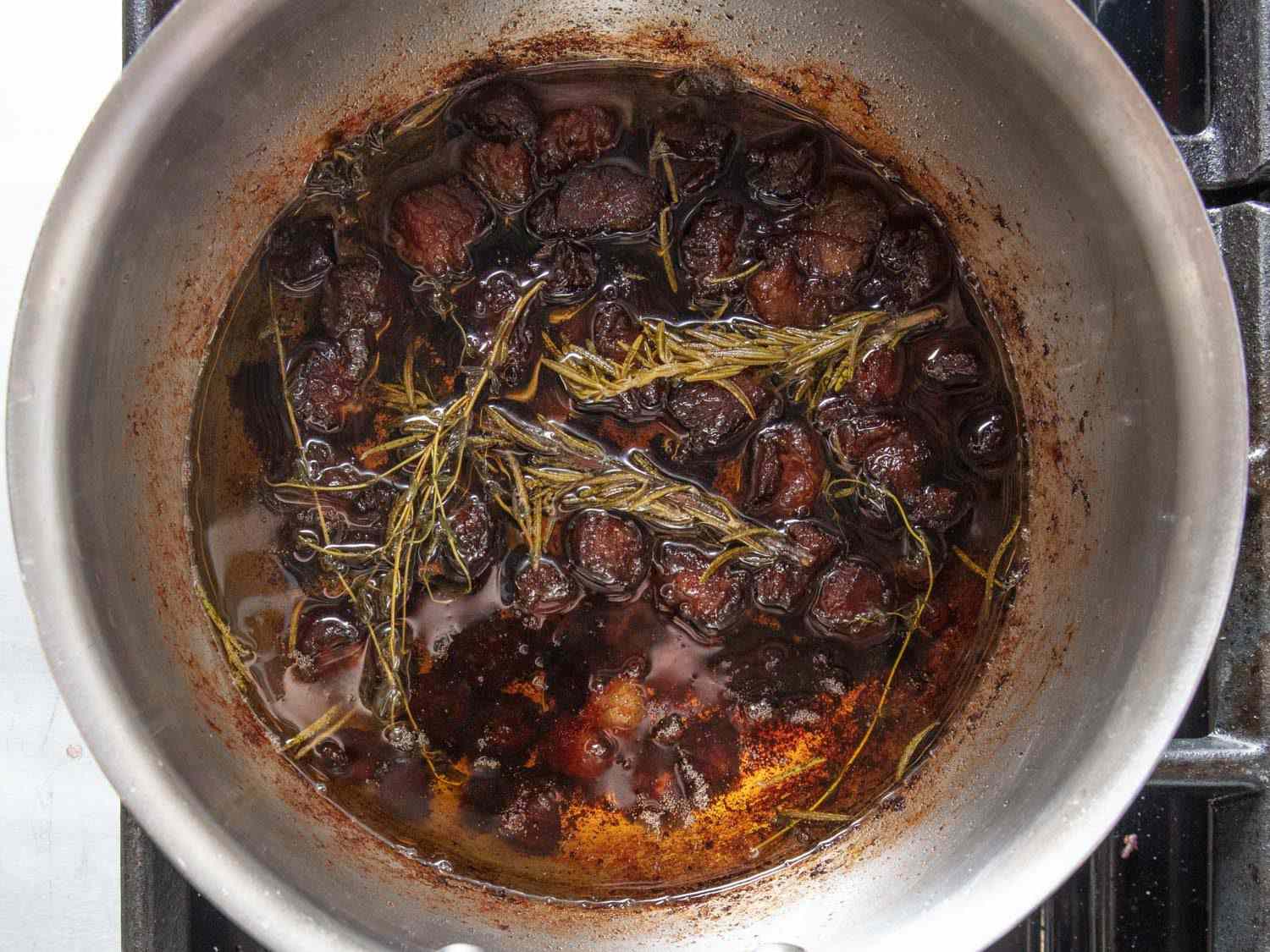 Closeup overhead of rendered dry-aged beef fat with rosemary in a saucepan.