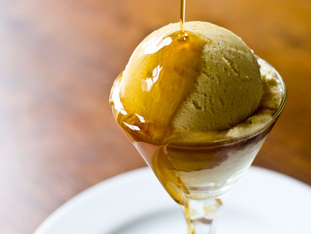 A scoop of maple ice cream in a coupe with maple syrup being drizzled on top. 