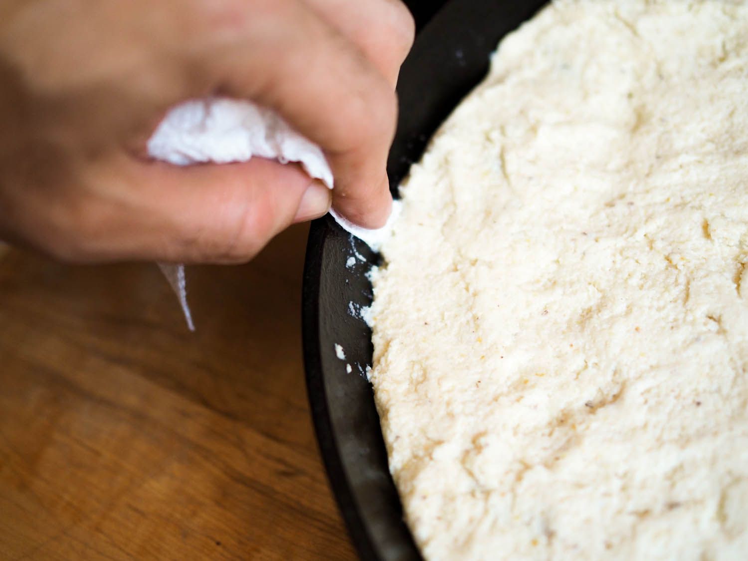 Author wiping the rim of the skillet with a kitchen towel, removing stray bits of masa dough.