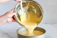 Batter being poured from a Vollrath mixing bowl into a round cake pan using a spatula