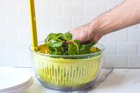 a person placing greens in the chef'n salad spinner