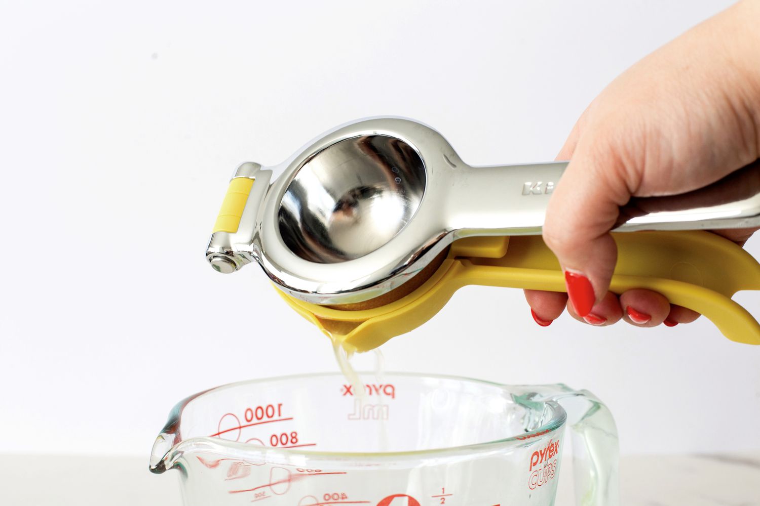 A person pouring citrus juicer from the KitchenAid citrus juicer into a measuring cup.
