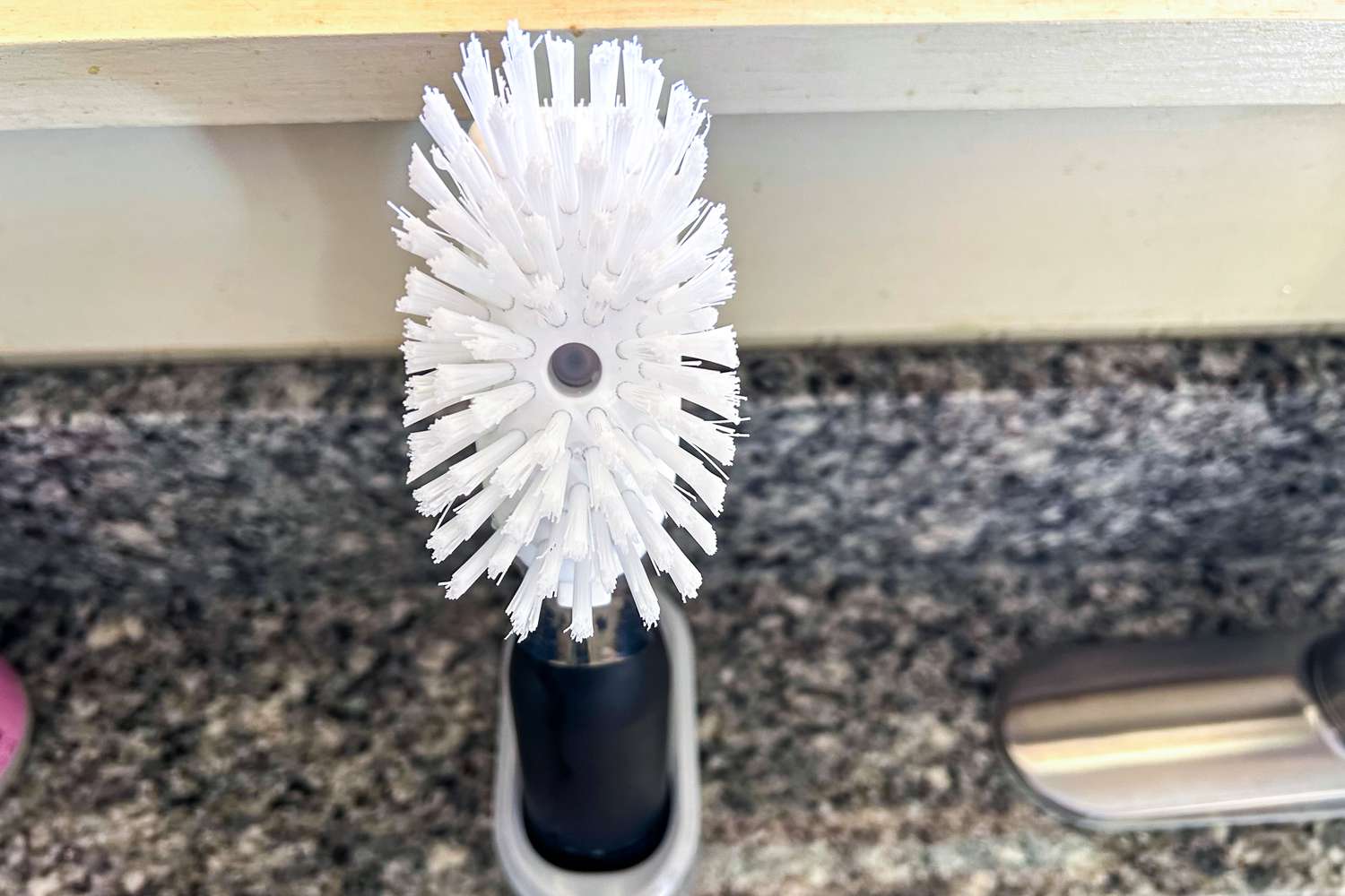 A closeup of an OXO dishwashing wand in a plastic holder next to a kitchen sink