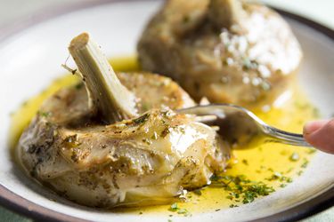 A plate of tender carciofi alla Romana. A fork easily cuts through a portion of one artichoke.