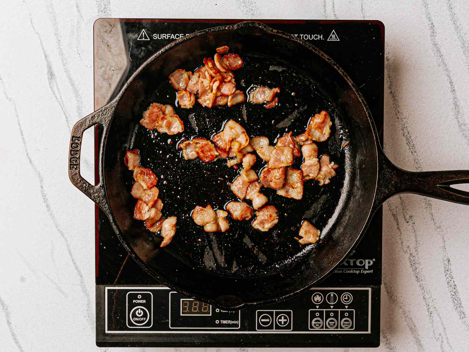 Chunks of meat cooking in a cast iron skillet on an induction stove