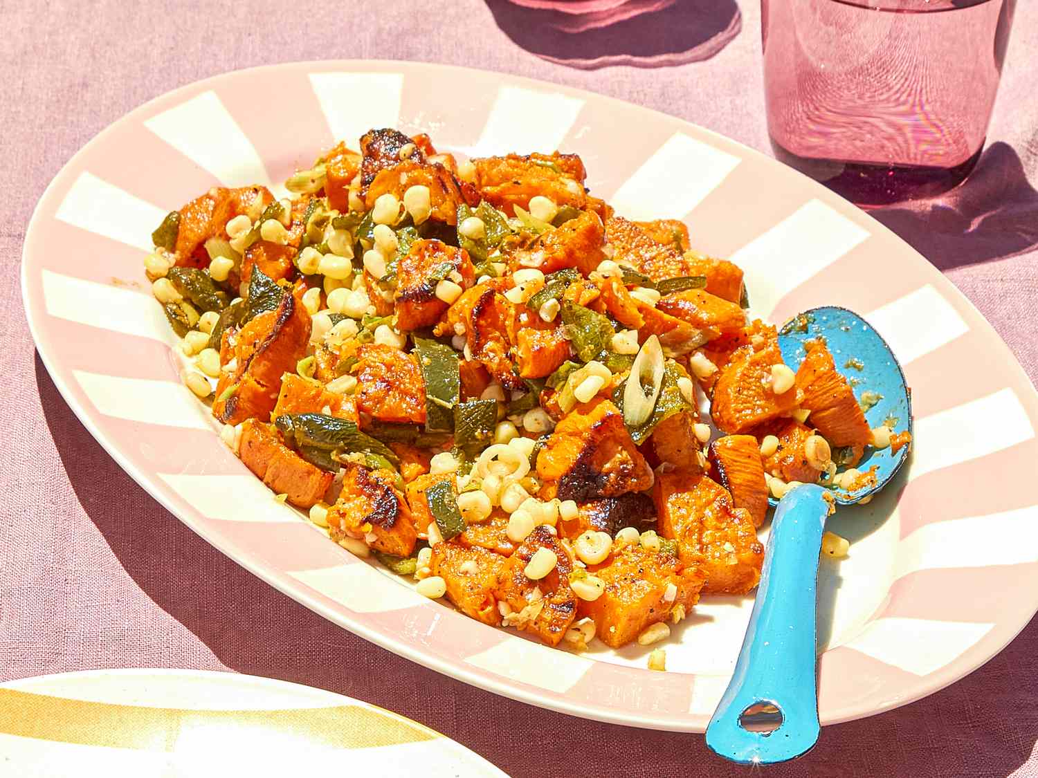 A platter containing grilled sweet potato and corn salad with a serving spoon