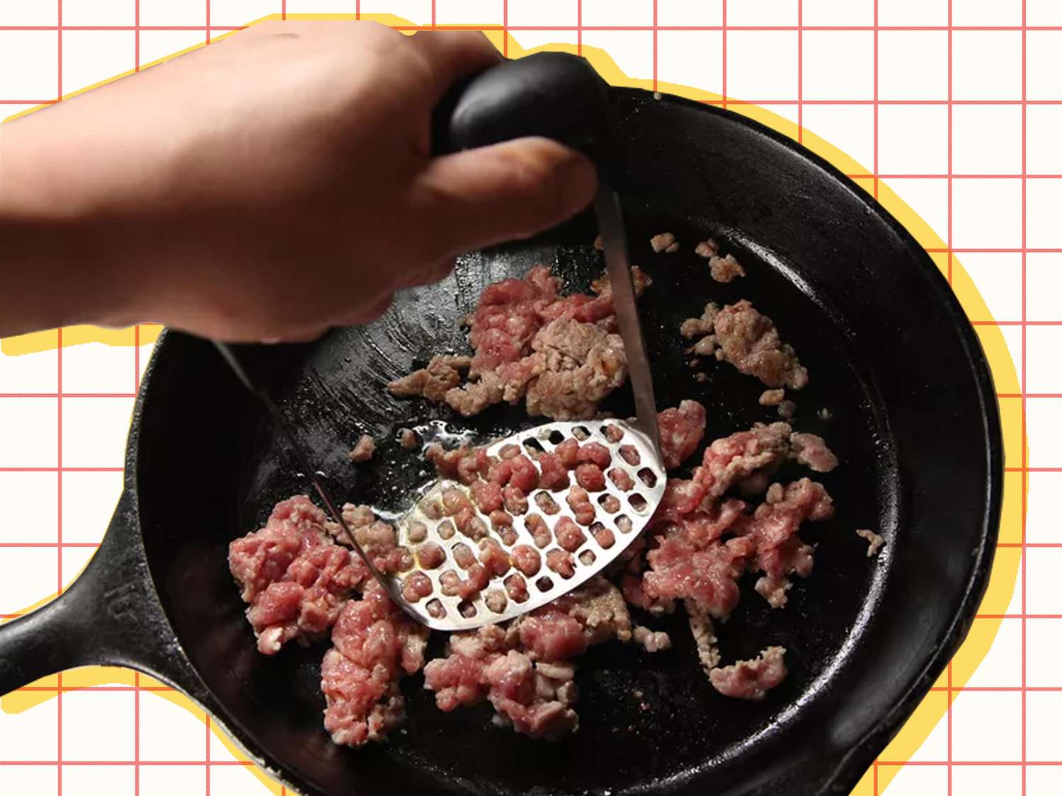 Smashing meat in a cast-iron skillet with a potato masher.