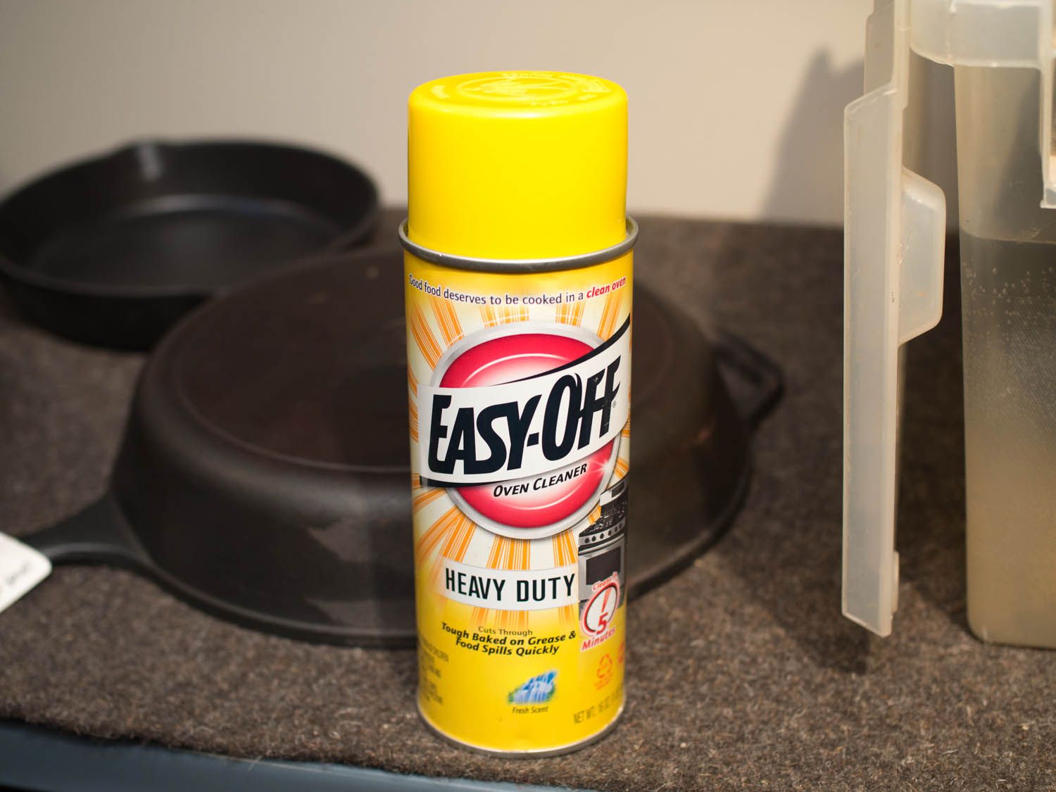 A can of 'Easy-off" heavy duty cleaner resting in front of a cast iron skillet. 