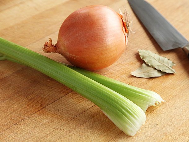 Celery stalks, a yellow onion, and two bay leaves on cutting board.