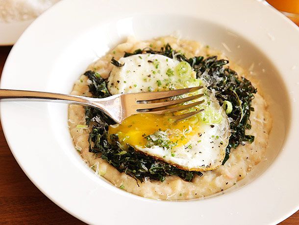 Fork puncturing fried egg on top of kale and creamy mashed white beans in shallow white bowl