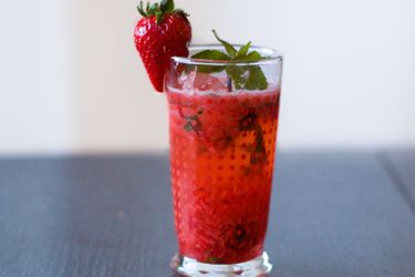 Profile view of a Strawberry Sake Cocktail, served in a tall glass with a sprig of mint and a whole strawberry gracing the rim.
