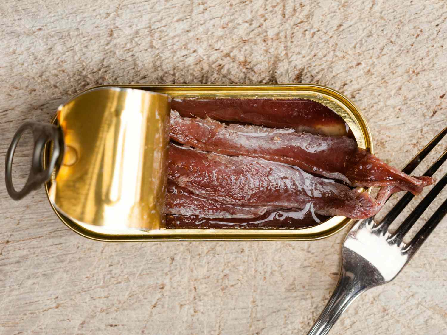 Overhead view of a tin of anchovies, partially opened to reveal the fillets inside.