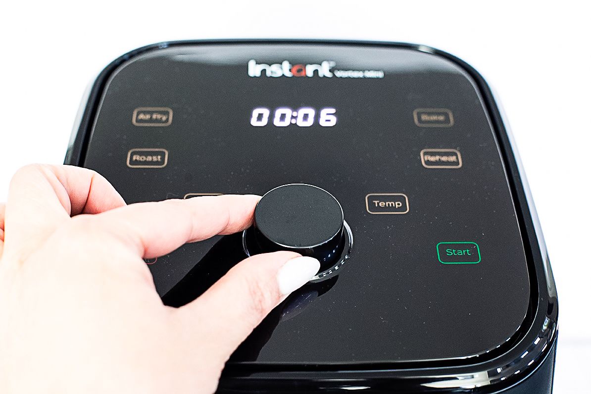 A persons hand adjusting the control knob on an Instant Vortex Mini appliance with a digital display showing 0006