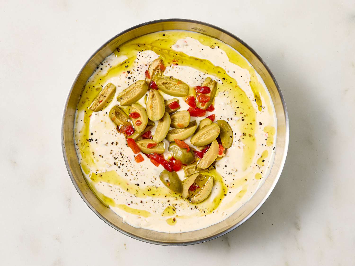 A bowl of dip garnished with sliced olives and seasoning