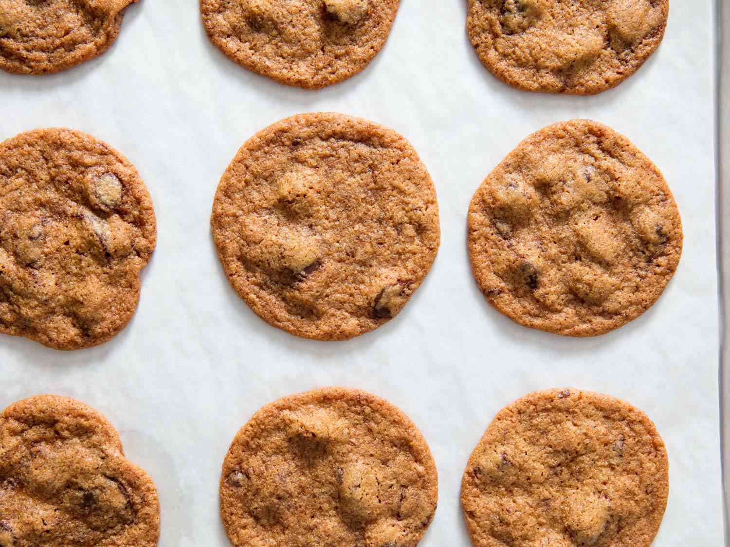 Overhead view of Tate's-style thin and crispy chocolate chip cookies on a parchment-lined baking sheet, fresh from the oven.