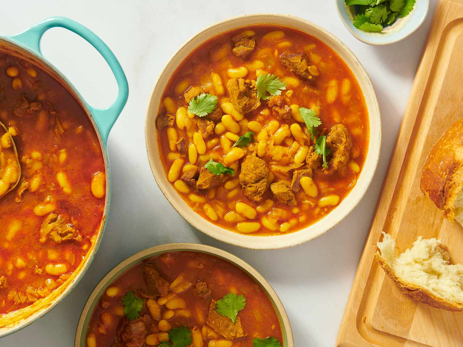 2 bowls of Moroccan white bean stew, with dutch oven of stew on the left, and wooden board with bread on the right 