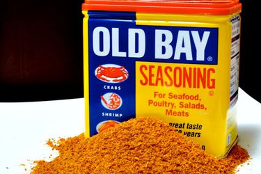 A tin of Old Bay seasoning with a pile of seasoning in front of it.