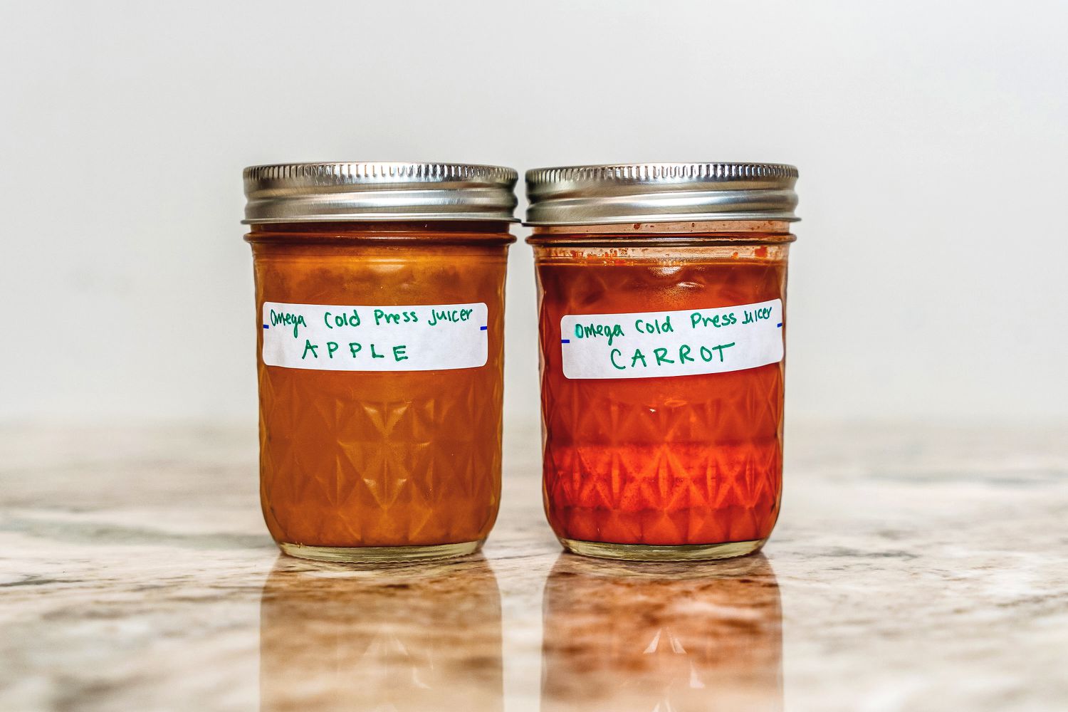 Two jars of cold pressed apple and carrot juice in mason jars on a granite counter