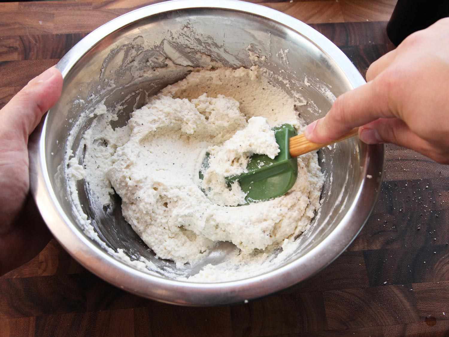 A spatula pressing the mixture of ricotta and grated Parmesan for gnudi until smooth. 