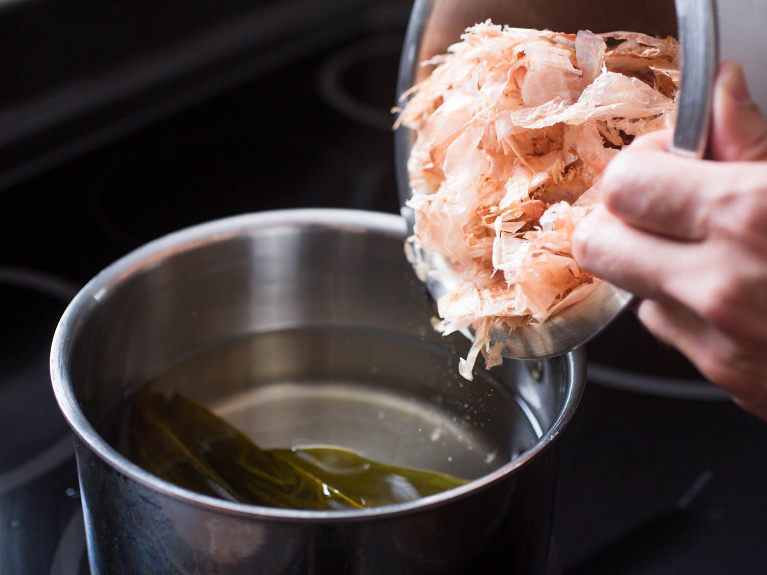 Kombu and bonito flakes are added to a saucepan full of water.